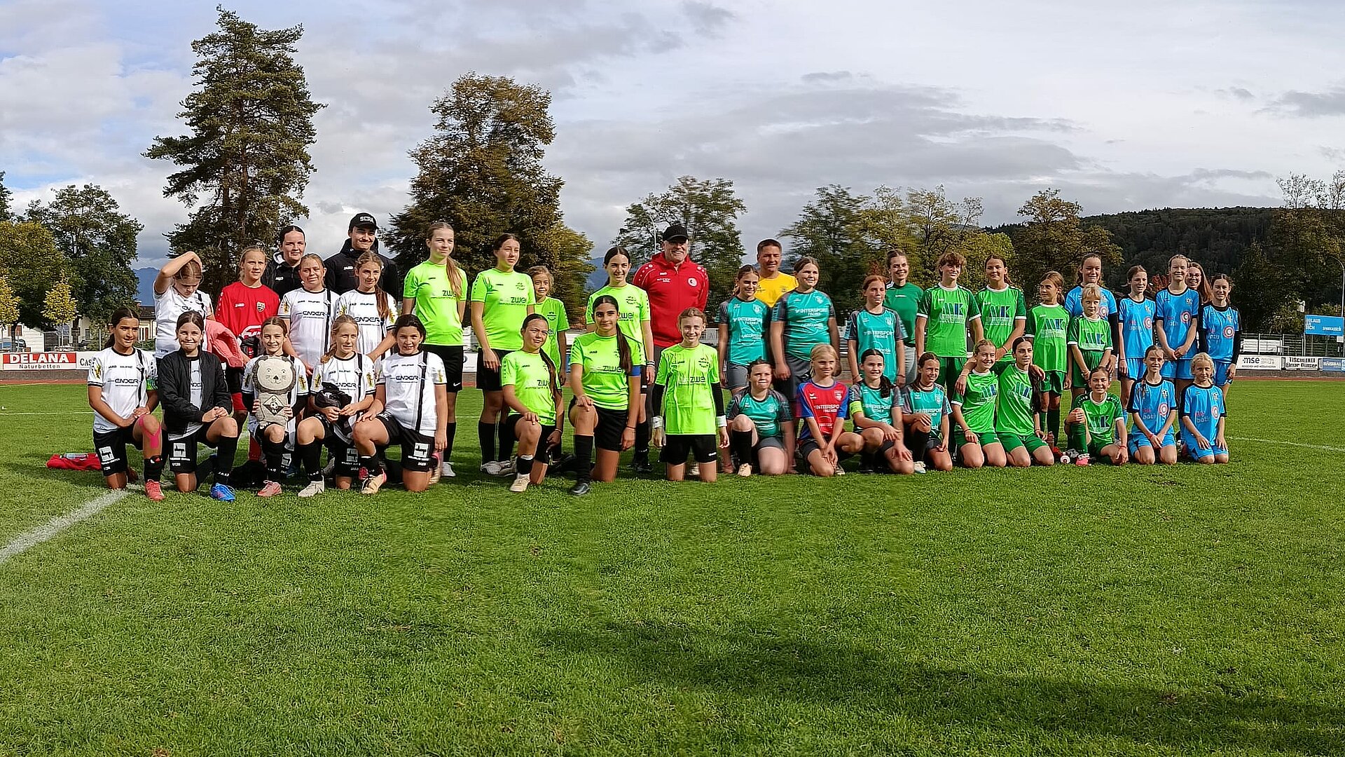 Fußballmannschaft mit Trainer*innen und Spielerinnen in Sportkleidung auf einem Rasenplatz