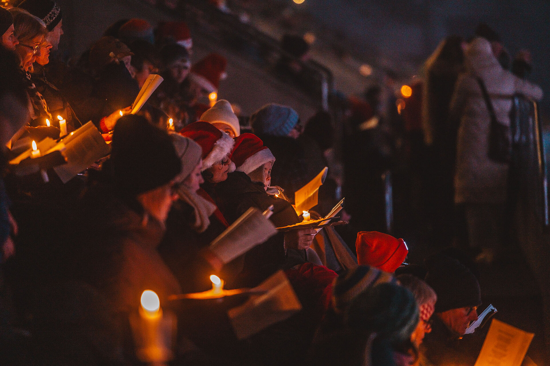 Chor mit Kerzen und Weihnachtsmützen in der Dunkelheit singend