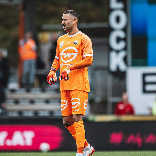Torhüter des SK Rapid Wien, mit orangenem Trikot und Handschuhen, auf dem Rasen