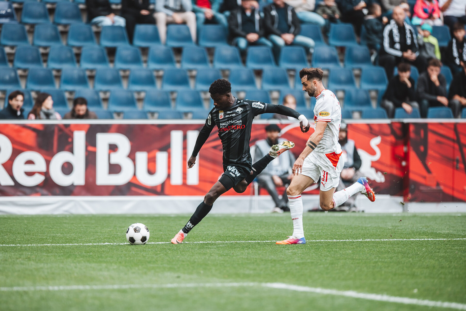 Fußballspieler in Schwarz-Weiß und Weiß-Rot dribbeln auf Rasen vor Red Bull Arena