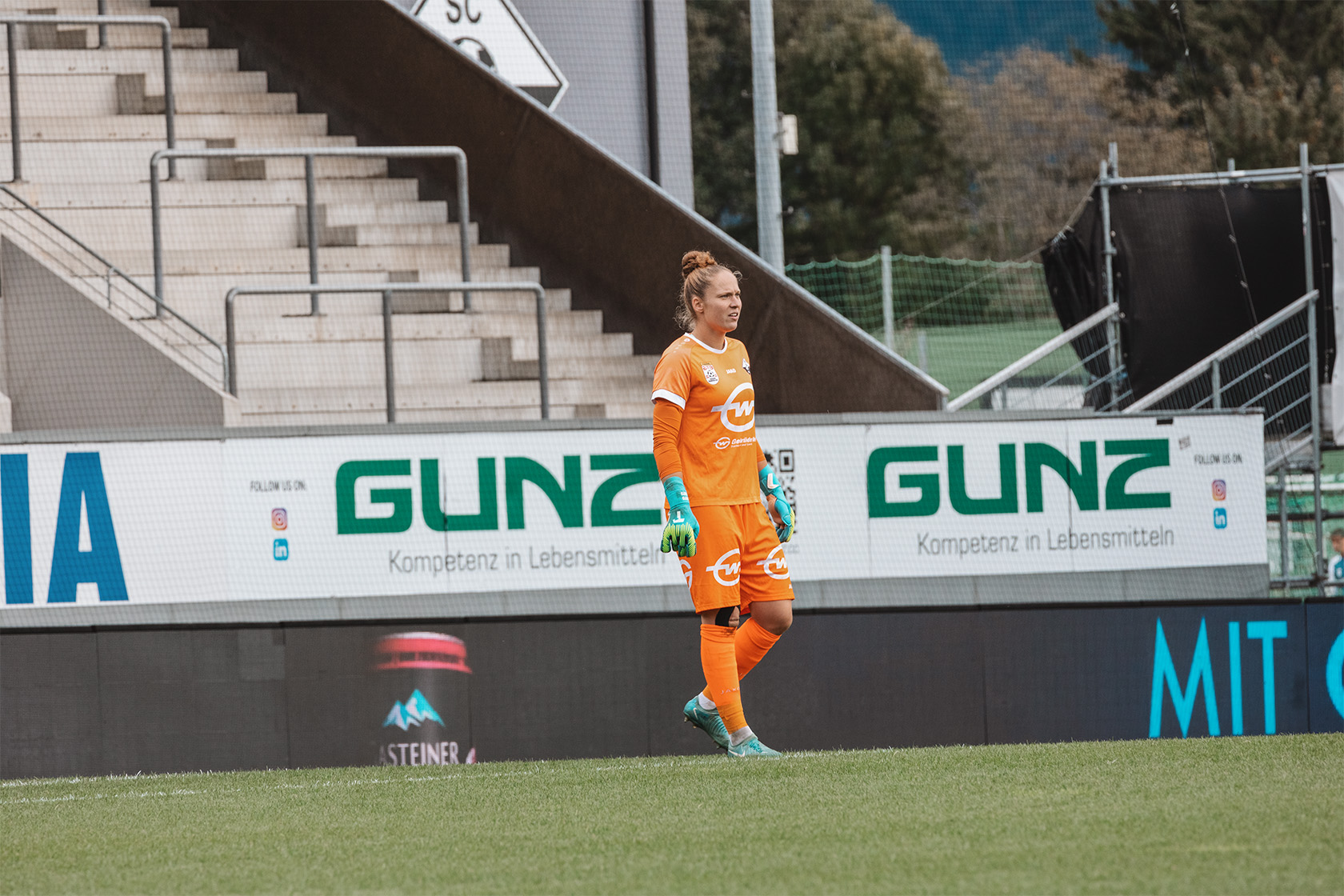 Torfrau im Fußballstadion mit Blick nach rechts, trägt orangefarbene Kleidung.