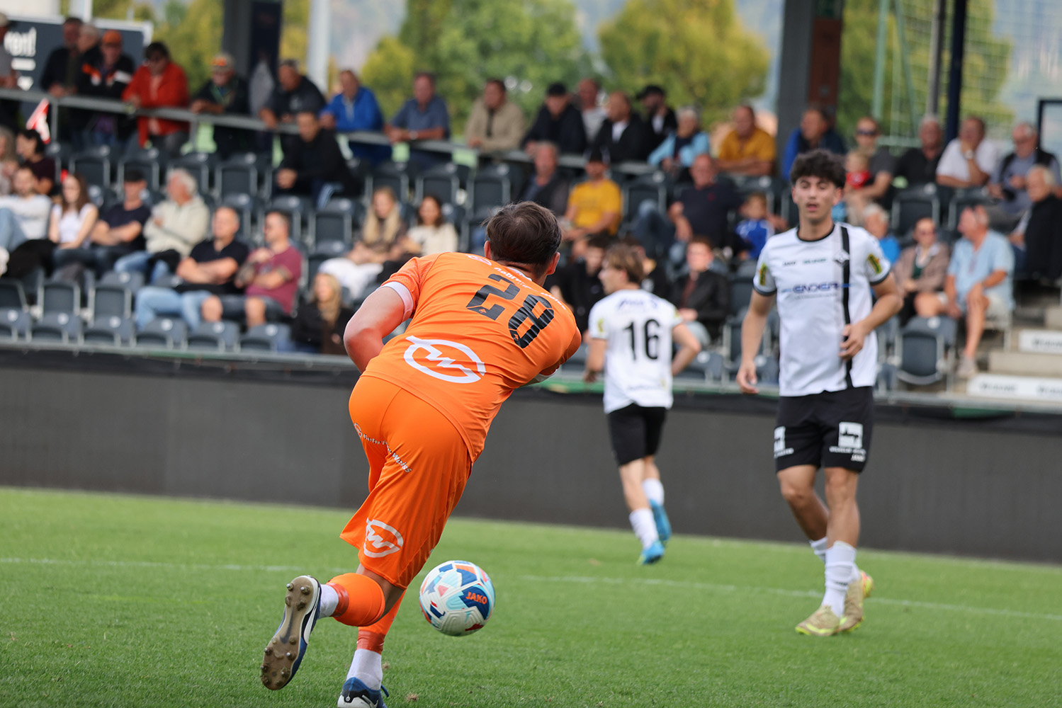 Fußballspieler in orange mit Ball am Fuß, Zuschauer im Hintergrund